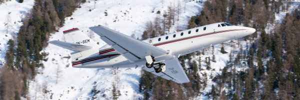 Ein Super Midsize Privatjet fliegt an einem beschneiten Gebiet entlang