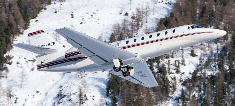 Ein Super Midsize Privatjet fliegt an einem beschneiten Gebiet entlang